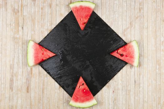 Triangular slices of watermelon on a black slate plate forming geometric games for copy space on a light wooden background