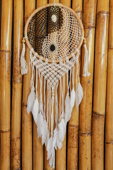 Dream catcher, decorated with white feathers and wooden beads, on a wooden surface. Dream catcher with wooden circle. Knitted Native American amulet with the symbol of Yin Yang on a bamboo background.