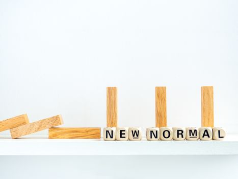 Social Distancing concept. Row of falling and standing wooden dominoes with distance space and New Normal, words on wooden alphabet cube on white background.
