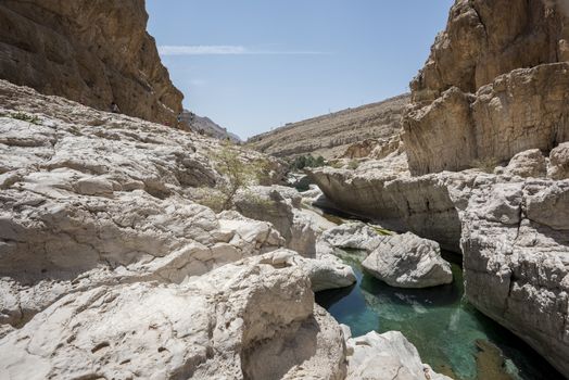 tourist beside the river (with turquoise water) and pool in the canyon of Wadi Bani Khalid, Sultanate of Oman