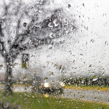 Blurry car silhouette seen through water drops on the car windshield.