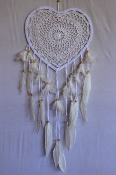 Dream catcher shaped heart with beige peacock feathers in the interior.