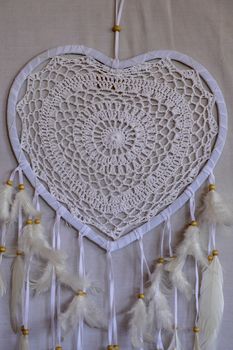 Dream catcher shaped heart with beige peacock feathers in the interior.