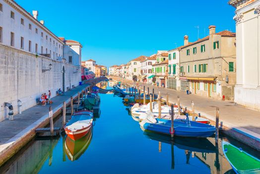 Chioggia - September 2016, Veneto, Italy: Canal with boats on water in Chioggia historic center. People are walking, sitting on benches near the old buildings and houses in Venetian style
