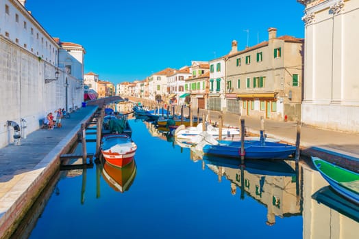 Chioggia - September 2016, Italy: Canal with boats on water in Chioggia historic center. People are walking along promenade, buildings and houses in Venetian style on the central street of the city