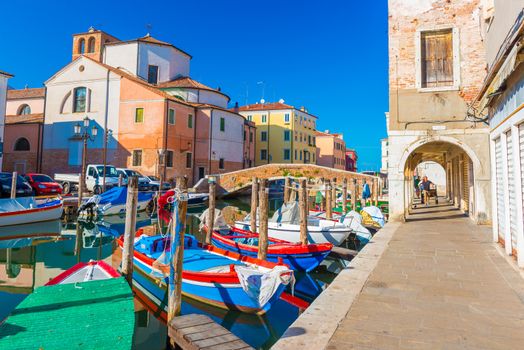 Chioggia - September 2016, Italy: Street of Chioggia, the town also known as a part of Venice. Boats lying on water in central canal "Vena". Old historical buildings and church against the blue sky