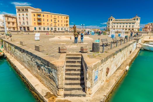 Syracuse - April 2019, Italy: Two tourists stand in front of The Archimedes Statue near Umbertino Bridge, which connects Syracuse and Ortygia