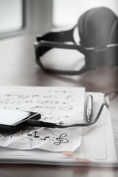 Closeup of smartphone with headphone on musical notes paper on wooden desk 