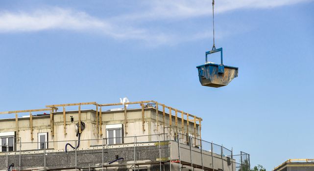 A blue container with building materials floats above the construction site with the shell of a large office building, germany