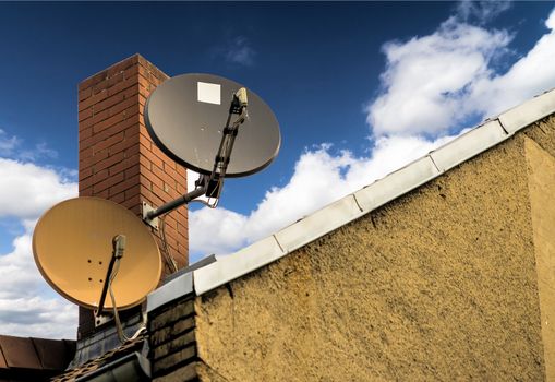 Two satellite dishes in front of a red brick chimney on the sloping roof of a house, germany