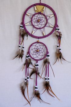 Red black and purple Dreamcatcher with bat made of feathers leather beads and ropes, hanging on the white background.