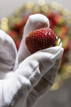 Hand of a man in a white glove holds a ripe strawberry with two fingers