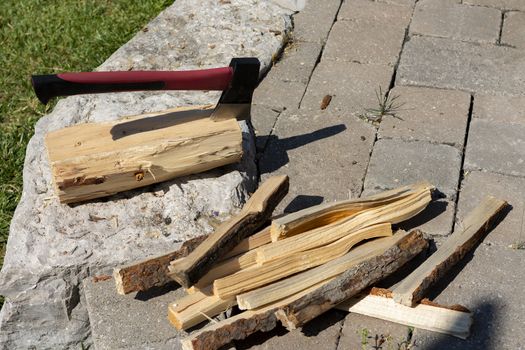 A pile of pine wood chips chopped from a large piece of a tree trunk to light a fire and an ax in a thick piece of wood