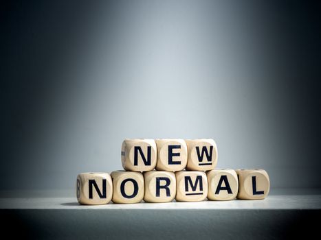 Spotlight shines on New Normal, words on wooden alphabet cube on dark background. New normal after covid-19 pandemic concept.