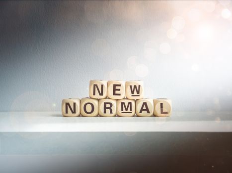 Beautiful bokeh from sunlight shines on New Normal, words on wooden alphabet cube on dark background. New normal after covid-19 pandemic concept.