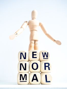 Close-up New Normal, words on wooden alphabet cube and wooden figure on white background, vertical style. New normal life after covid-19 pandemic concept.