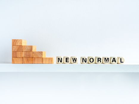 Stairs down to New Normal, words on wooden alphabet cube on shelf on white background with copy space. New normal after covid-19 pandemic concept.