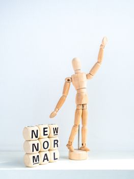 New Normal, words on wooden alphabet cube and wooden figure raising up hand on white background, vertical style. New normal life after covid-19 pandemic concept.