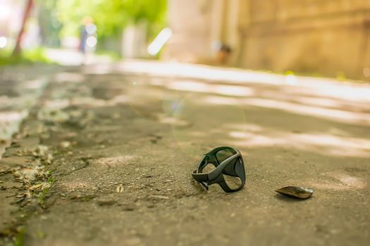 broken lost sunglasses with a broken glass are lying on the sidewalk of a city street against the background of passing pedestrians, people