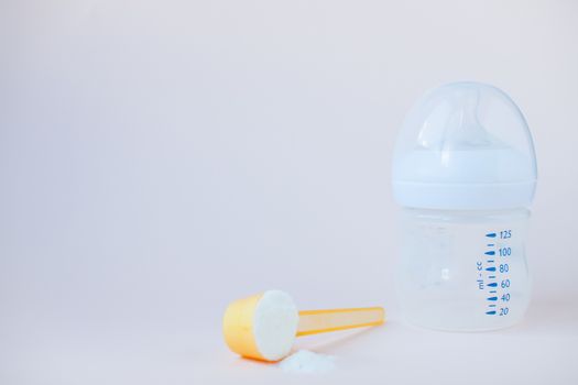 Artificial feeding of babies. Bottle for the mixture, measuring spoon, dry milk adapted mixture. Silicone rodent in pastel colors. Copy space for text.