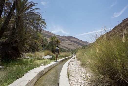 Woman walking near an artificial canal with water in the famous Wadi Bani Khalid in the Sultanate of Oman