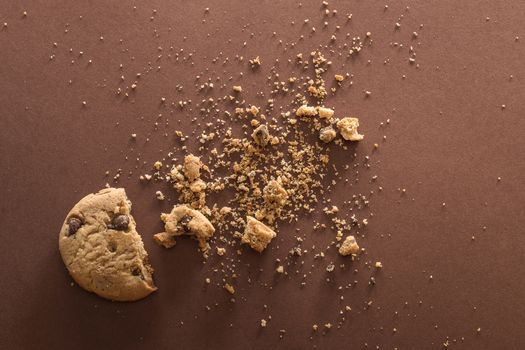 Broken chocolate chip cookie on brown background. Top view. Copy space.