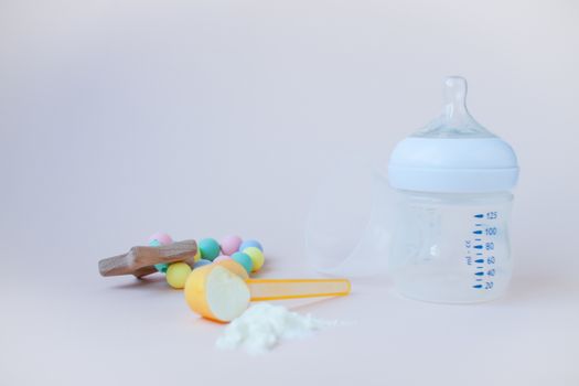 Artificial feeding of babies. Bottle for the mixture, measuring spoon, dry milk adapted mixture. Silicone rodent in pastel colors. Copy space for text.