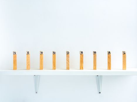 New normal and social distancing concept. New Normal, words on wooden alphabet cube on row of wooden dominoes with distance space on shelf on white background.