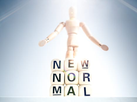 New Normal, words on wooden alphabet cube and wooden figure on white background with sparkle light. New normal life after covid-19 pandemic concept.