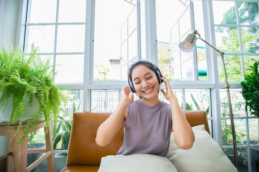 Asian women wearing headphones and using laptop and digital tablet for Listening to music and singing on a relaxing day at home
