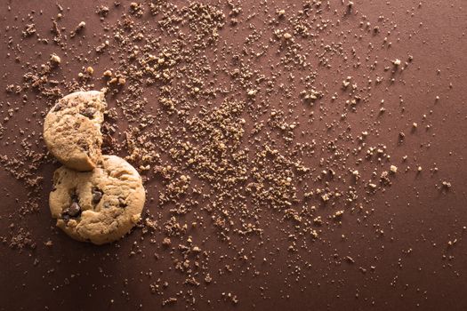 Broken chocolate chip cookies on brown background. Top view. Copy space.