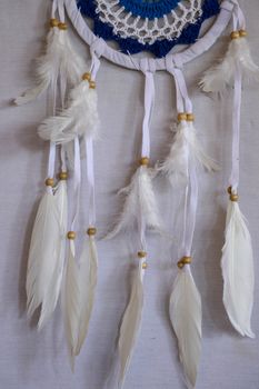 Handmade pink dream catcher with white doily on background of rocks and lake. Tribal elements, feathers, lace, crochet snowflake.