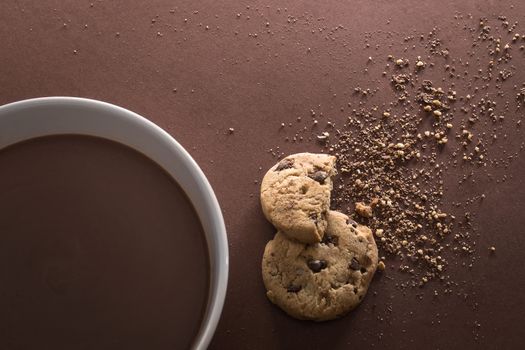Chocolate white bowl and broken chocolate chip cookies on brown background. Top view. Copy space.