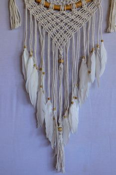 Handmade pink dream catcher with white doily on background of rocks and lake. Tribal elements, feathers, lace, crochet snowflake.