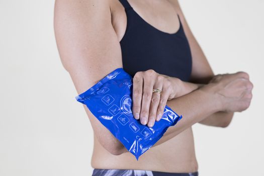 Woman with sportswear using Cold Instant Pack on her elbow on white cream background
