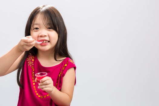 Young girl happily eating cup of gelatin dessert on isolated white background.