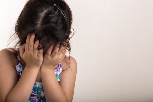 Little girl is covering her face with her hands because of fear.