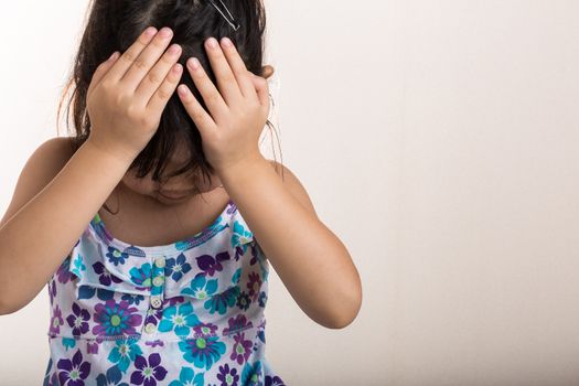 Little girl covers her forehead with hands when feeling disappointed.