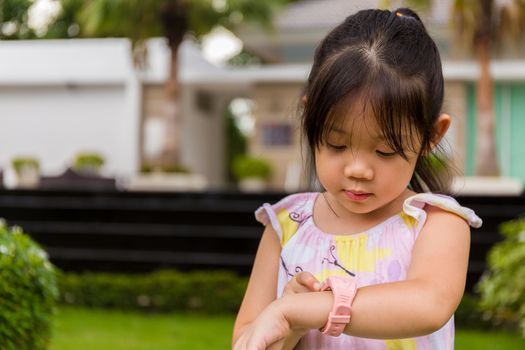 Child standing in garden using smartwatch or smart watch on her wrist.