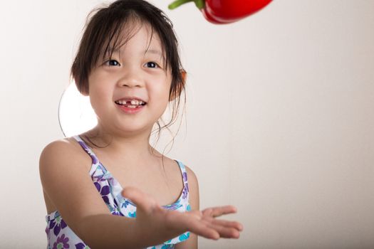 Little girl is throwing a red bell pepper in the air.