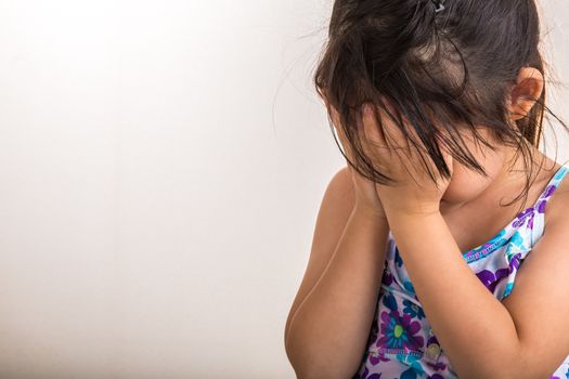 Little girl is playing hind-and-seek by covering her face with hands.