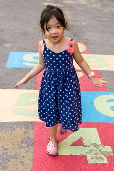 Young girl playing hopscotch on playground with happiness.