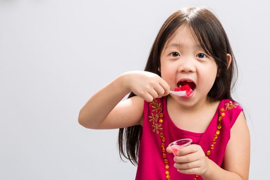 Young girl happily eating cup of gelatin dessert on isolated white background.