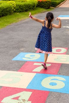 Young girl playing hopscotch on playground with happiness.