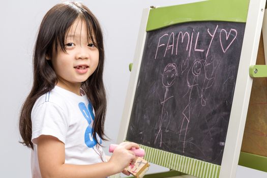 Little kid sit beside a blackboard studio isolated.