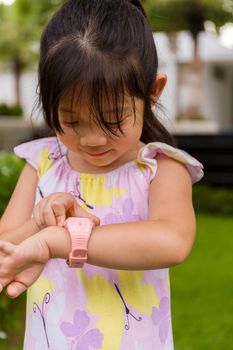 Child standing in garden using smartwatch or smart watch on her wrist.