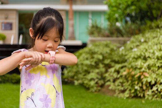 Child standing in garden using smartwatch or smart watch on her wrist.