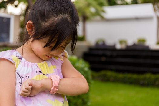 Child standing in garden using smartwatch or smart watch on her wrist.