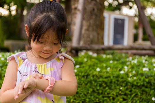 Child standing in garden using smartwatch or smart watch on her wrist.