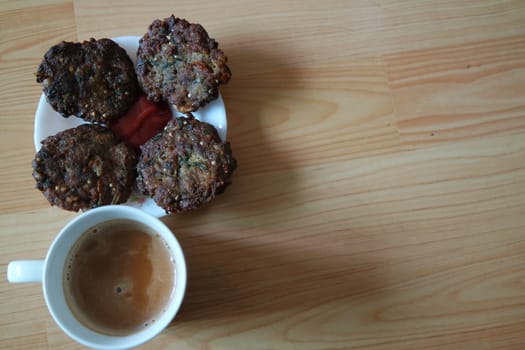 Delicious spicy fried round kebab served in white ceramic plate on a wooden floor with cup of hot tea.